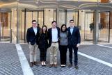 Image: A group of students standing a front of a building's glass entrance. The sign "Deloitte" is visible inside the building.